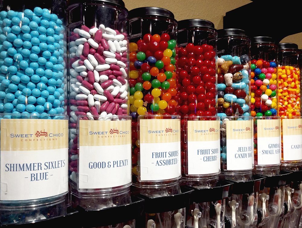 Rows of clear bulk candy dispensers filled with colorful sweets like Good & Plenty, fruit sours, jelly beans, and gumballs