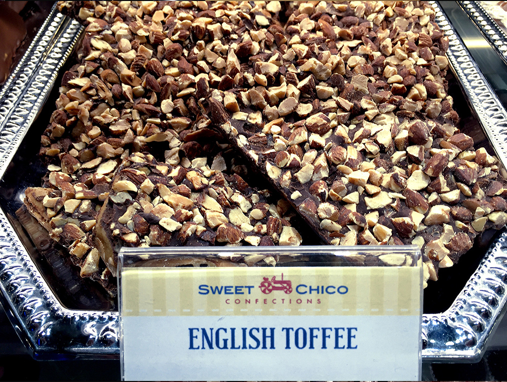 House-made English toffee topped with chopped nuts displayed in a case at Sweet Chico Confections