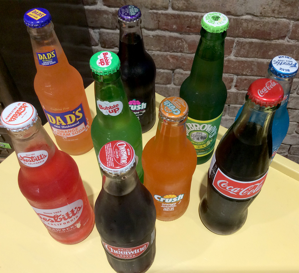 Assorted vintage glass bottle sodas including Dad’s, Bubble Up, Crush, Nehi, and Coca-Cola on display at Sweet Chico Confections